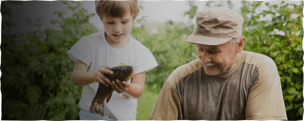 Adult Man And Child Holding Fish Outdoors By Water